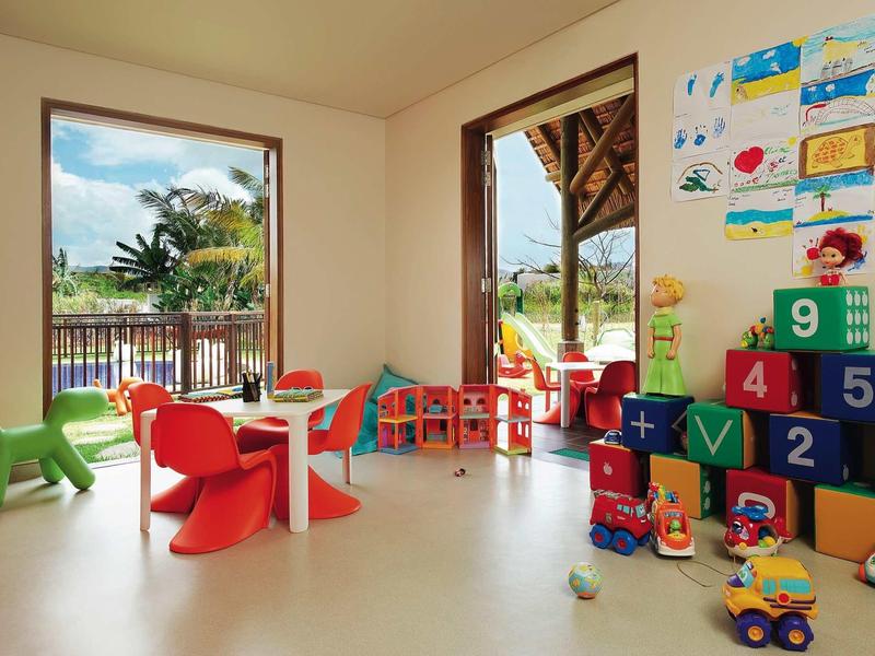 Jasny pokój zabaw dla dzieci z kolorowymi krzesłami, zabawkami i tarasem z widokiem na zewnątrz.