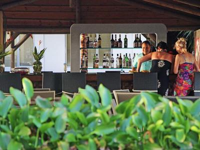 Bar aperta con posti a sedere e ospiti circondati da piante verdi.