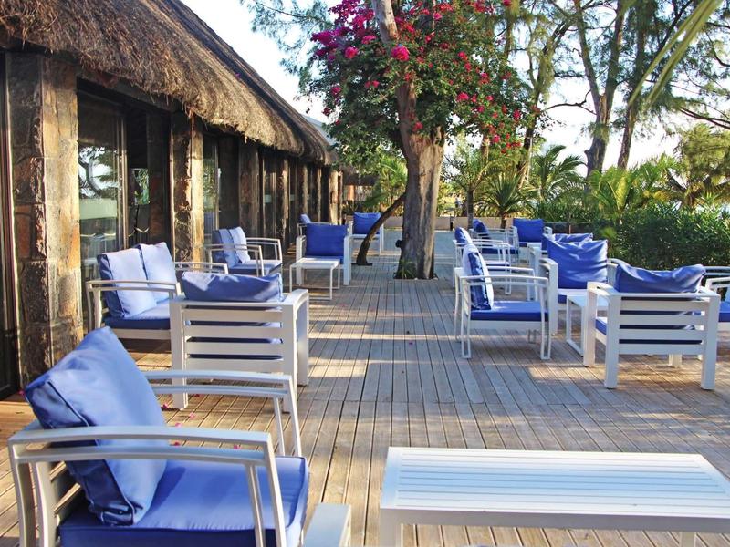 Terrasse avec des chaises bleues et des tables le long d'un bâtiment dans un jardin.