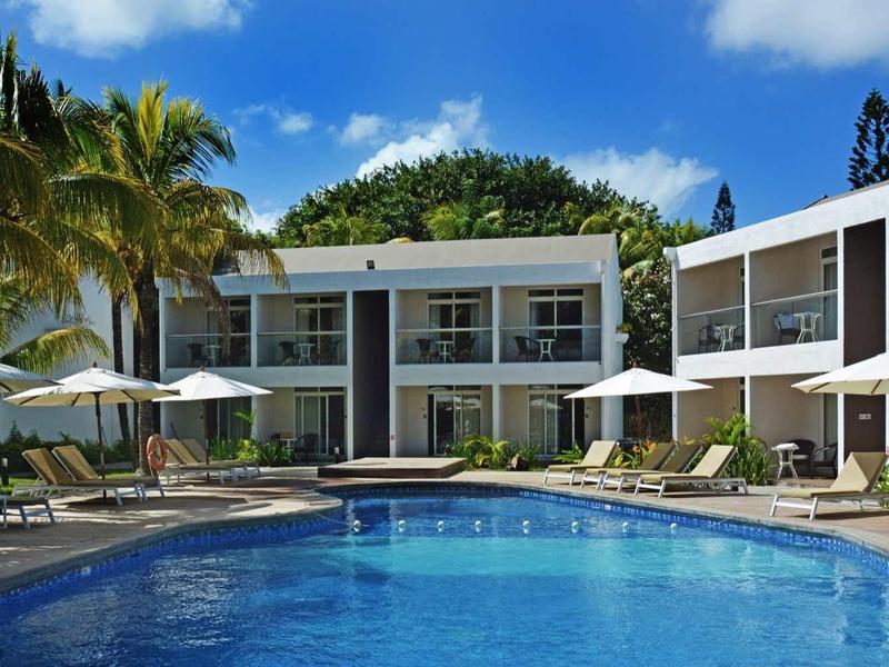 Piscine d'hôtel moderne avec chaises longues, parasols et verdure sous un ciel bleu.