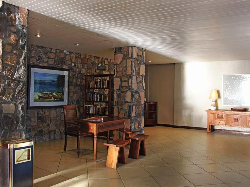 Hall d'hôtel avec colonnes en pierre, meubles en bois et étagères à livres sous lumière naturelle.