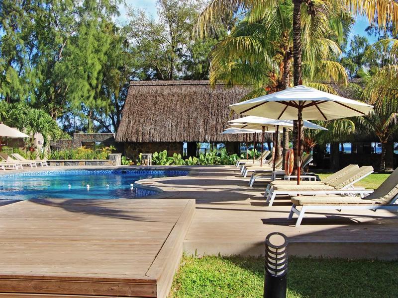 Espace piscine détendu avec chaises longues et parasols dans un cadre tropical.