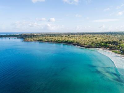 Clear blue ocean meets sandy beach with green forested coastline.
