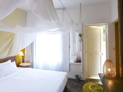 Brightly decorated hotel room with white bed and open wooden doors to the bathroom.
