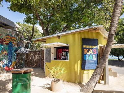 Small yellow beach kiosk with trees and colorful graffiti on the wall.