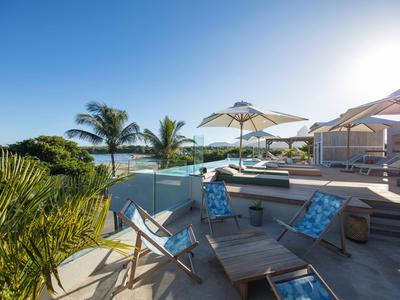 Modernes Hotelpool-Areal mit Liegestühlen, Sonnenschirmen und Palmen bei klarem Himmel.