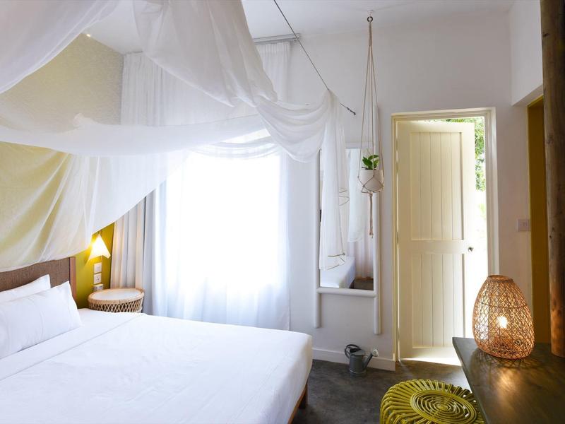 Brightly decorated hotel room with white bed and open wooden doors to the bathroom.