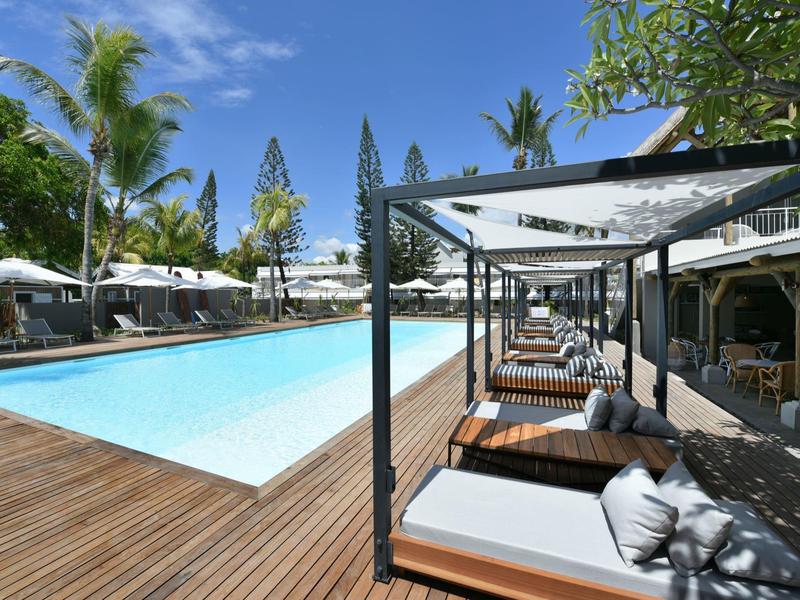Luxurious pool area with loungers and umbrellas, surrounded by palm trees and blue sky.