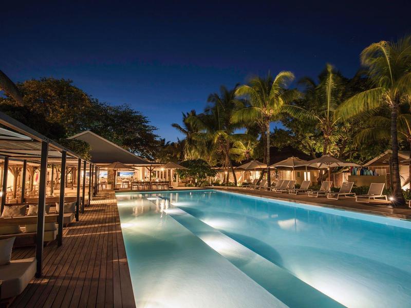Illuminated swimming pool with loungers and palm trees at a hotel at night