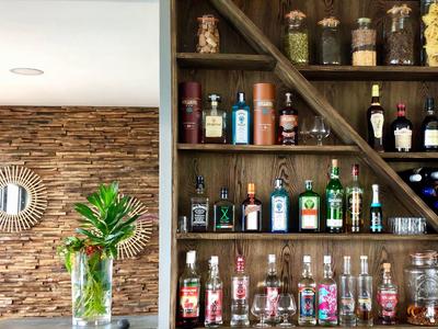 Holzregal mit Spirituosenflaschen, links Wand mit Steinoptik und Spiegel, Vase mit grünen Pflanzen.