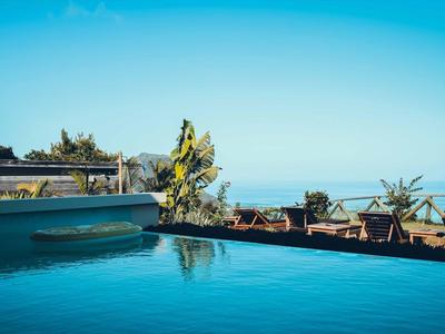 Schwimmbecken mit blauem Wasser, umgeben von Palmen und klar blauem Himmel im Hintergrund.