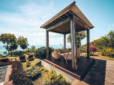 Offene Holzhütte in tropischem Garten mit Blick auf das Meer am sonnigen Tag.