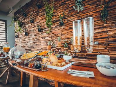 Buffet-Tisch mit verschiedenen Frühstücksoptionen vor einer Steinwand mit hängenden Pflanzen.