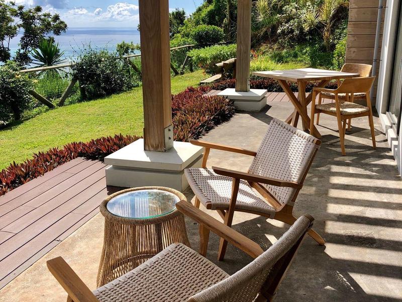 Terrasse mit Holzstühlen, runden Tischen und Blick auf grünen Garten unter blauem Himmel.