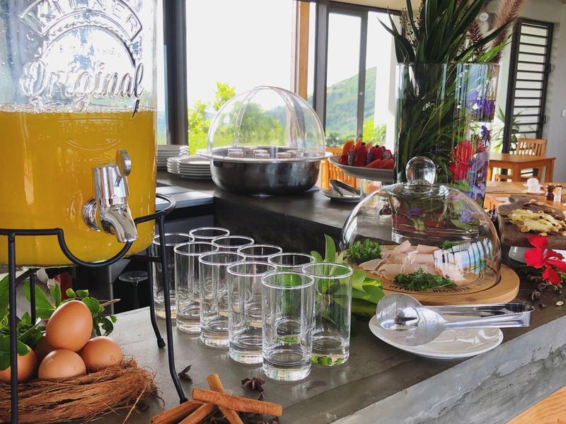 Frühstücksbereich mit Saftspender, Eiern, Gläsern, Gebäck und Gewürzen auf grauer Arbeitsfläche.