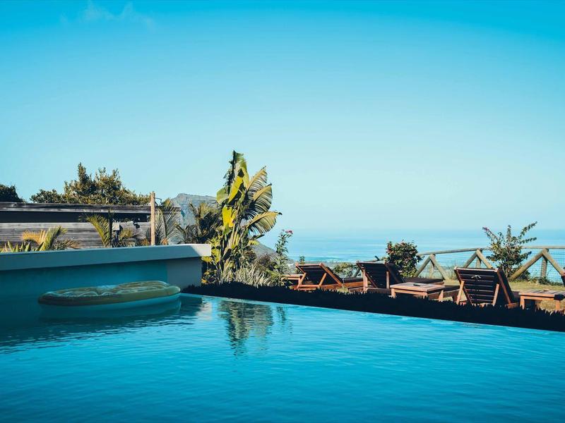 Schwimmbecken mit blauem Wasser, umgeben von Palmen und klar blauem Himmel im Hintergrund.