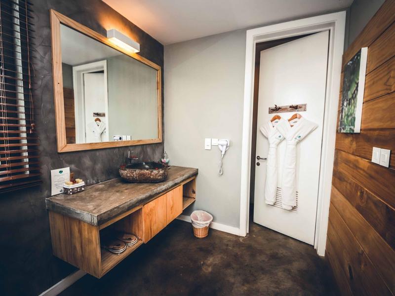 Modernes Badezimmer mit hölzernem Waschbecken, großem Spiegel und weißen Bademänteln an der Tür.