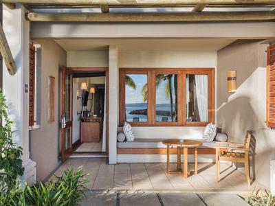 Gemütliche Terrasse eines Hotels mit Holzmöbeln und Blick auf Palmen und Meer.