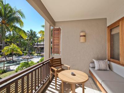Balkon mit Sitzgelegenheiten und Tisch, Blick auf Pool und Palmen in sonniger Hotelanlage.