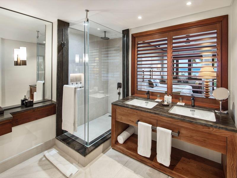 Modernes Badezimmer mit Glaskabine, Holzwaschtisch und großen Spiegeln in einem Hotelzimmer.