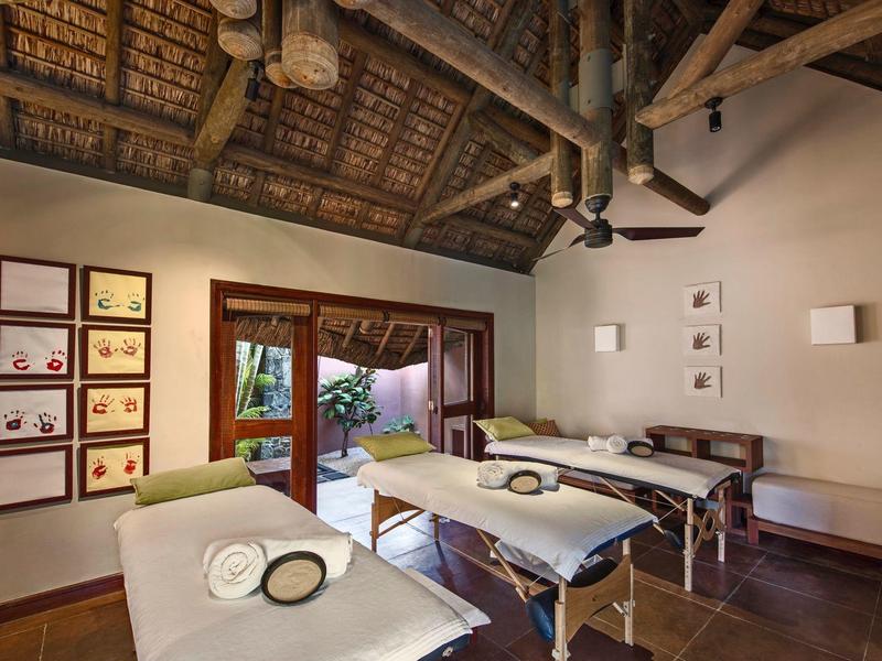 Ruheraum mit zwei Massageliegen, Holzdecke, Ventilator und großen Fenstern zum Garten.