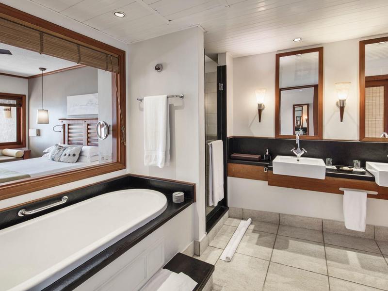 Moderne Badezimmer mit großer Badewanne, Doppelwaschbecken, Spiegeln und weißem Fliesenboden.