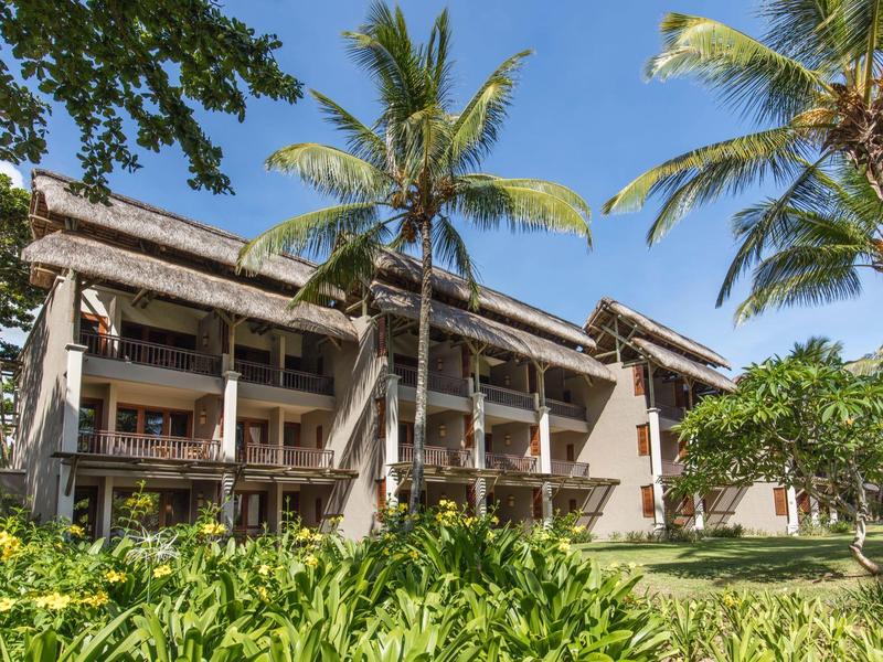 Mehrstöckiges Hotelgebäude mit Balkonen, umgeben von Palmen und üppigem Grün bei blauem Himmel.