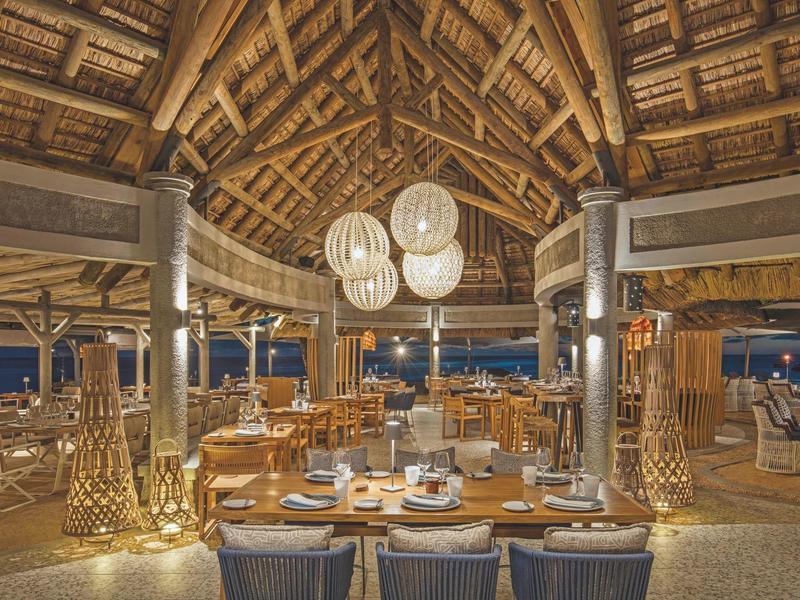 Offenes Restaurant mit Holzdecke, großen Lampen und eleganten, gedeckten Tischen bei Nacht.