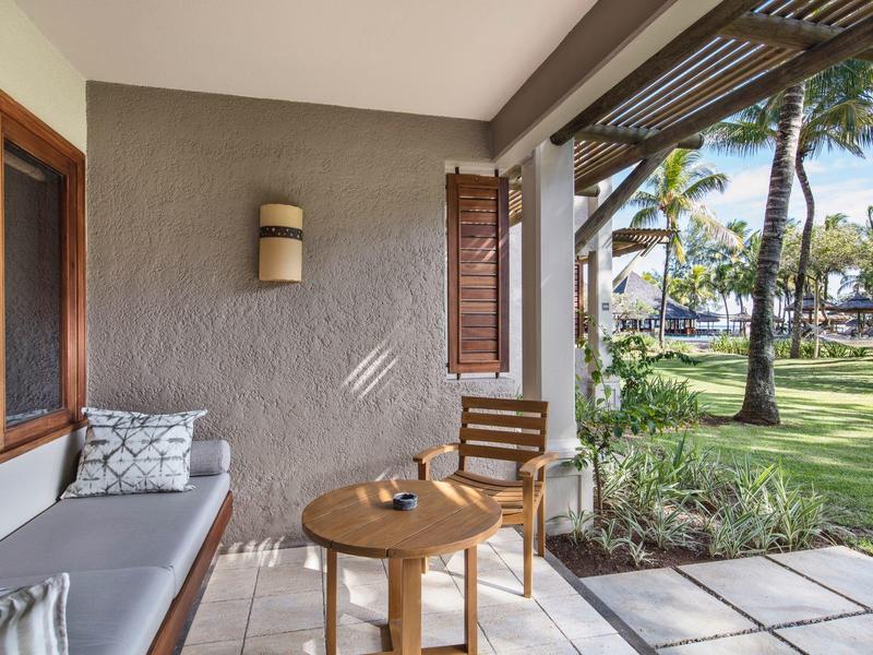 Terrasse mit Holztisch, Stuhl und Sofa mit Kissen, Blick auf tropischen Garten mit Palmen.