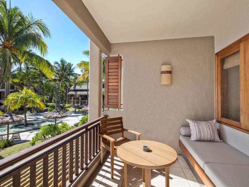 Balkon mit Holzmöbeln und Blick auf tropischen Garten und Pool bei sonnigem Wetter.