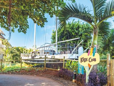 Przystań z żaglówką i znakiem Kids Club obok palm pod niebieskim niebem