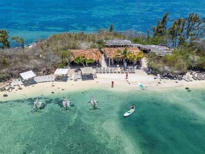 Mały ośrodek na wyspie z plażą, kilkoma chatkami i łodziami na czystej wodzie.