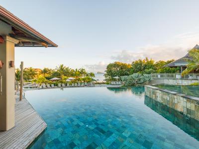 Piscina a sfioro con vista su alberi tropicali e aree per ospiti sotto un cielo azzurro.