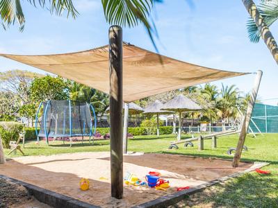 Piaskownica z osłoną przeciwsłoneczną i zabawkami w ogrodzie z palmami i trampoliną