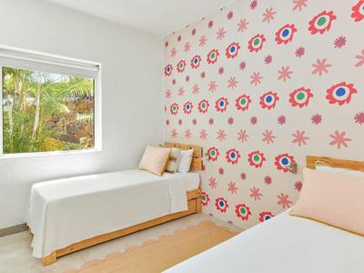 Jasna sypialnia z dwoma pojedynczymi łóżkami i kolorową dekoracyjną ścianą.