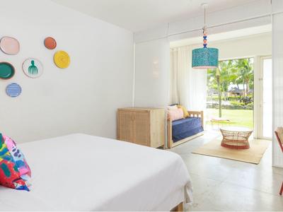 Jasny pokój hotelowy z podwójnym łóżkiem, kolorowymi dekoracjami na ścianach i częścią wypoczynkową z dostępem do ogrodu.