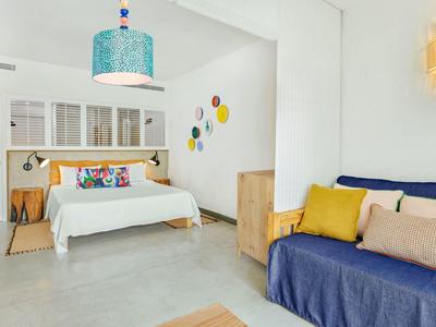 Jasny, nowoczesny pokój hotelowy z łóżkiem podwójnym, niebieską sofą i kolorową dekoracją ściany.