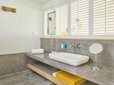 Nowoczesne lustro łazienkowe z umywalką, szarym blatem i białymi żaluzjami w oknie.