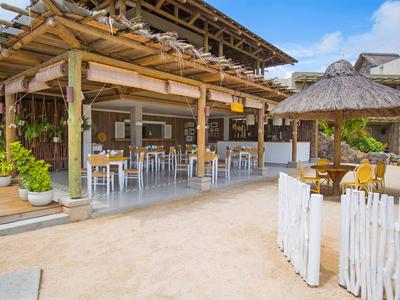 Ristorante aperto con tetto in legno e tavoli su sabbia sotto il cielo azzurro