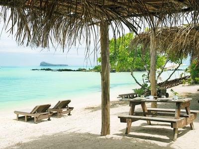 Plaża z drewnianymi leżakami, stolikiem piknikowym i widokiem na morze pod strzechą.