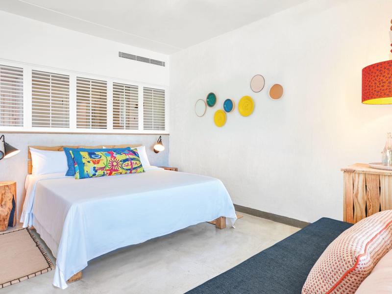 Nowoczesny pokój hotelowy z wygodnym łóżkiem, kolorowymi poduszkami i prostą dekoracją ścian.