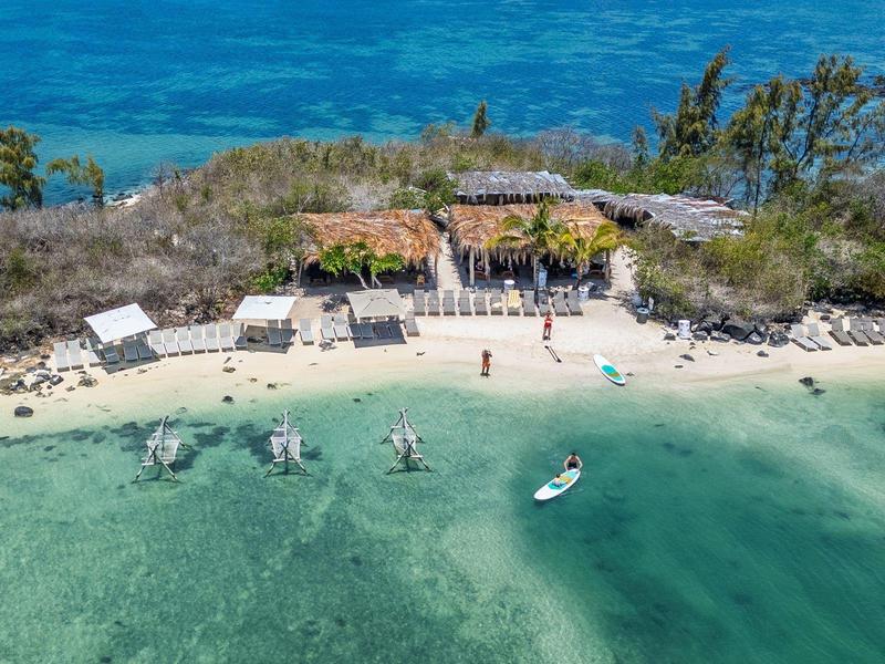 Mały ośrodek na wyspie z plażą, kilkoma chatkami i łodziami na czystej wodzie.