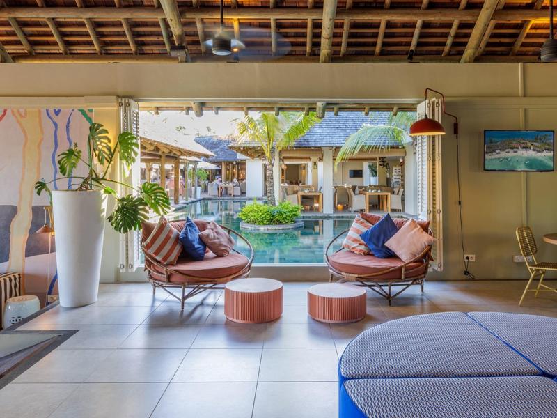 Otwarta przestrzeń lounge z miejscami do siedzenia z widokiem na ogród i basen w hotelu tropikalnym.