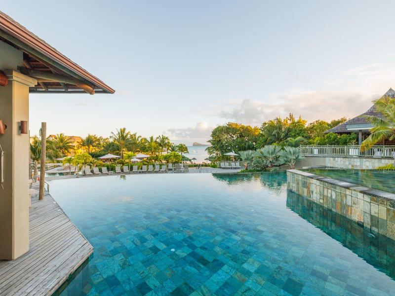 Basen infinity z widokiem na tropikalne rośliny i spokojne niebo w ośrodku.