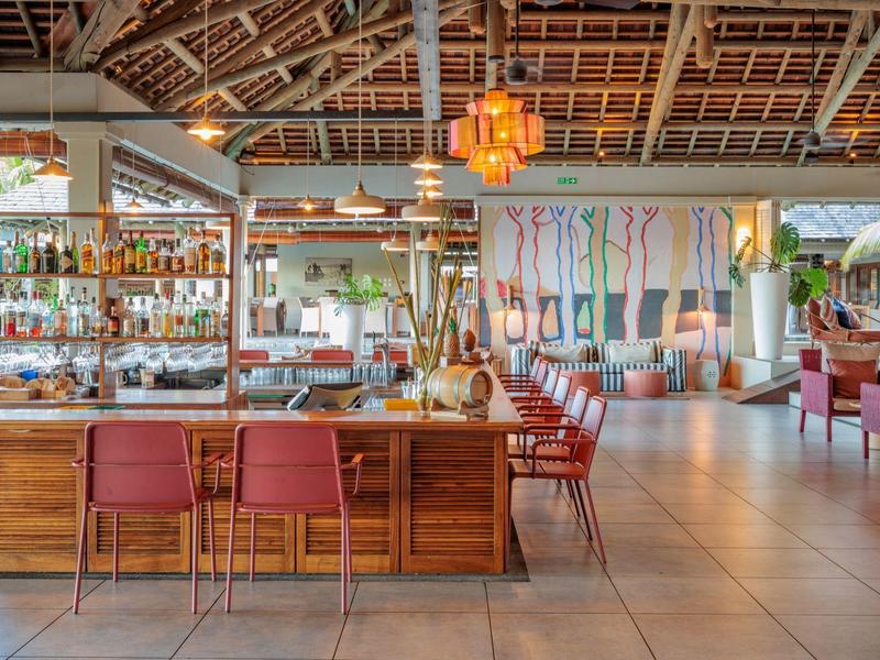 Otwarty bar hotelowy z czerwonymi krzesłami, drewnianymi elementami i ciepłym oświetleniem