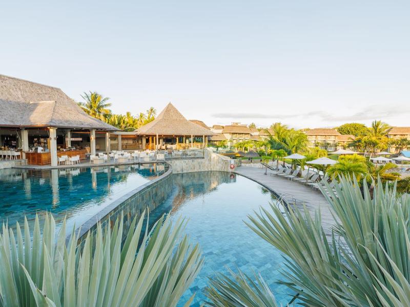 Widok na tropikalny basen z palmami i dachami ze strzechy w ośrodku.