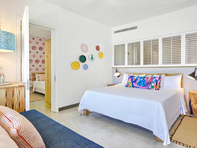 Jasny, nowoczesny pokój hotelowy z dużym łóżkiem, kolorowymi poduszkami i dekoracyjną ścianą.