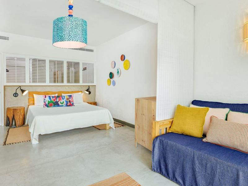 Jasny, nowoczesny pokój hotelowy z łóżkiem podwójnym, niebieską sofą i kolorową dekoracją ściany.