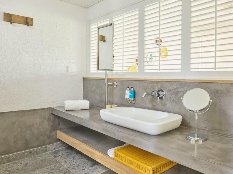 Nowoczesne lustro łazienkowe z umywalką, szarym blatem i białymi żaluzjami w oknie.