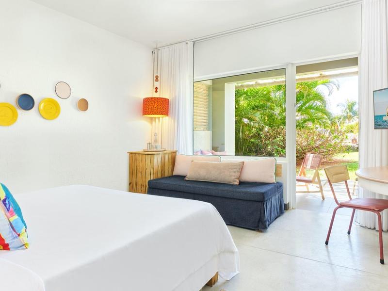 Jasny pokój hotelowy z łóżkiem podwójnym, sofą, biurkiem i przesuwnymi drzwiami na taras i ogród.